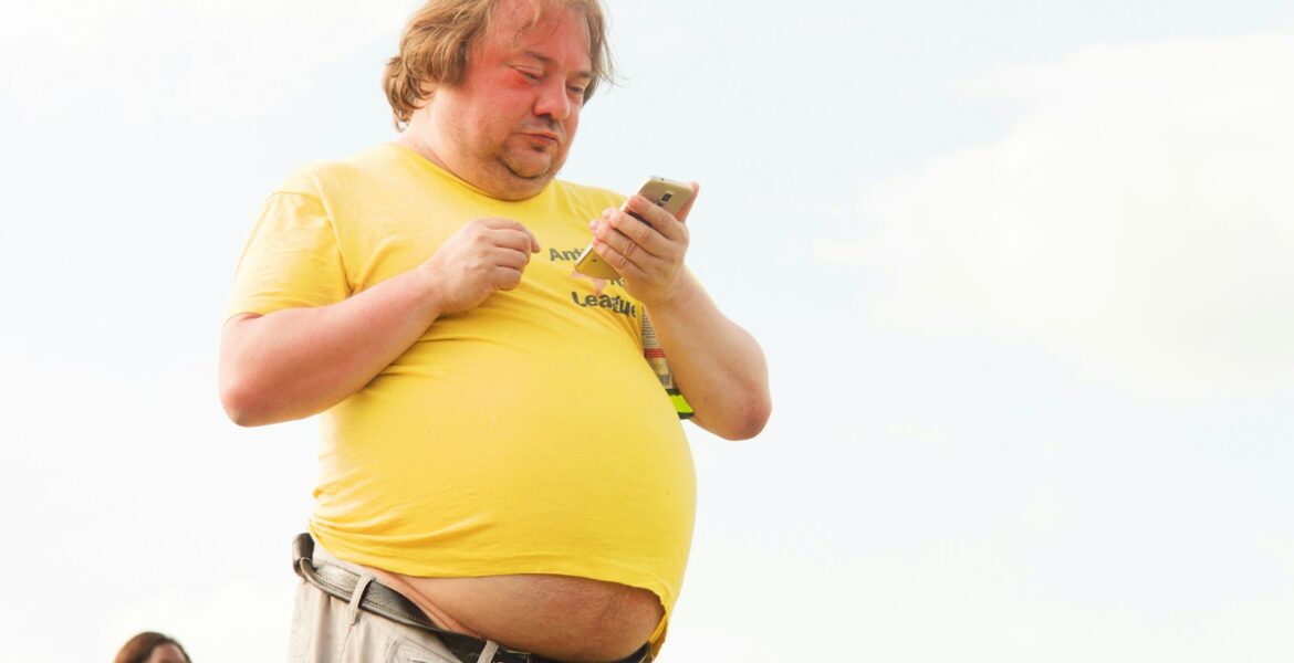 man in yellow shirt and brown pants using smartphone